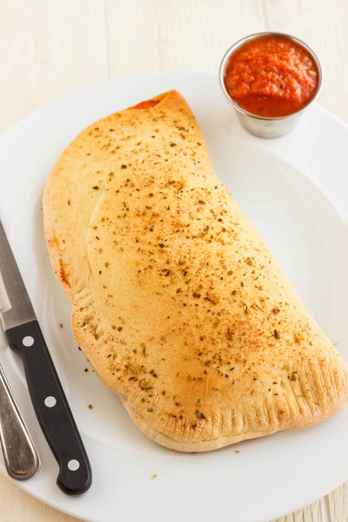 Homemade Calzones on white tray with knife and fork with small bowl with dip