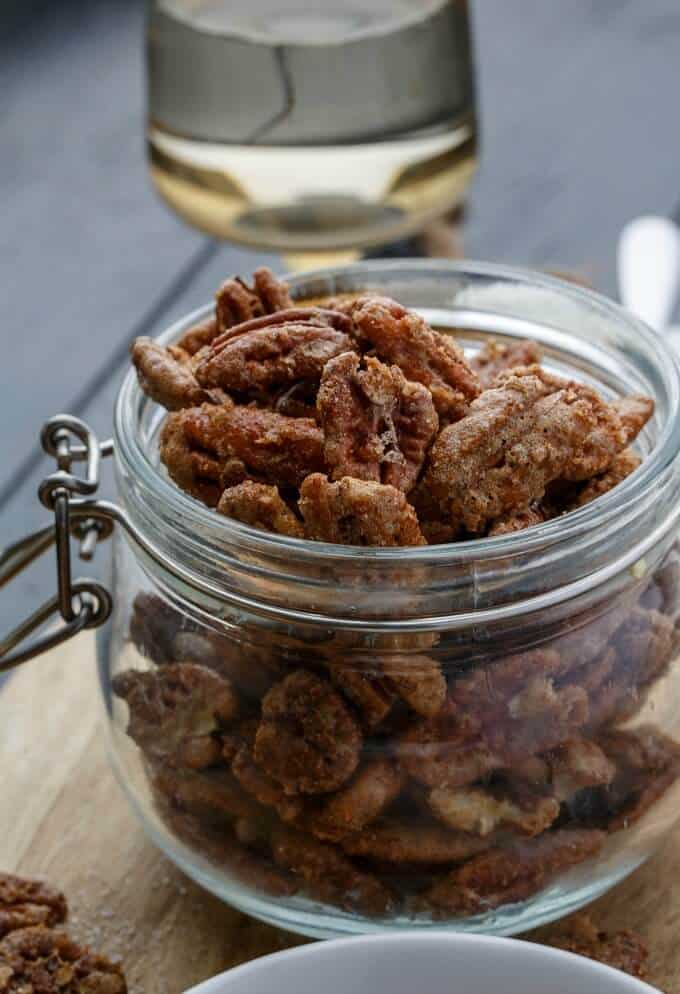 Spicy Glazed Pecans in glass jar on wooden pad, glass of wine in the background