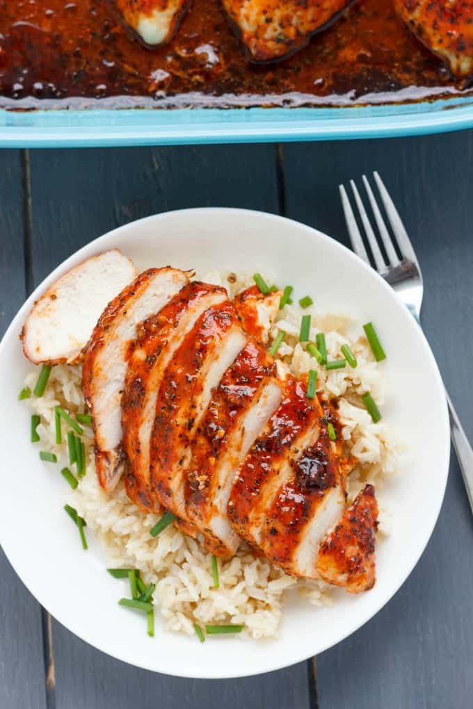 Sriracha sliced chicken breast with rice and veggies on white plate on gray table with fork