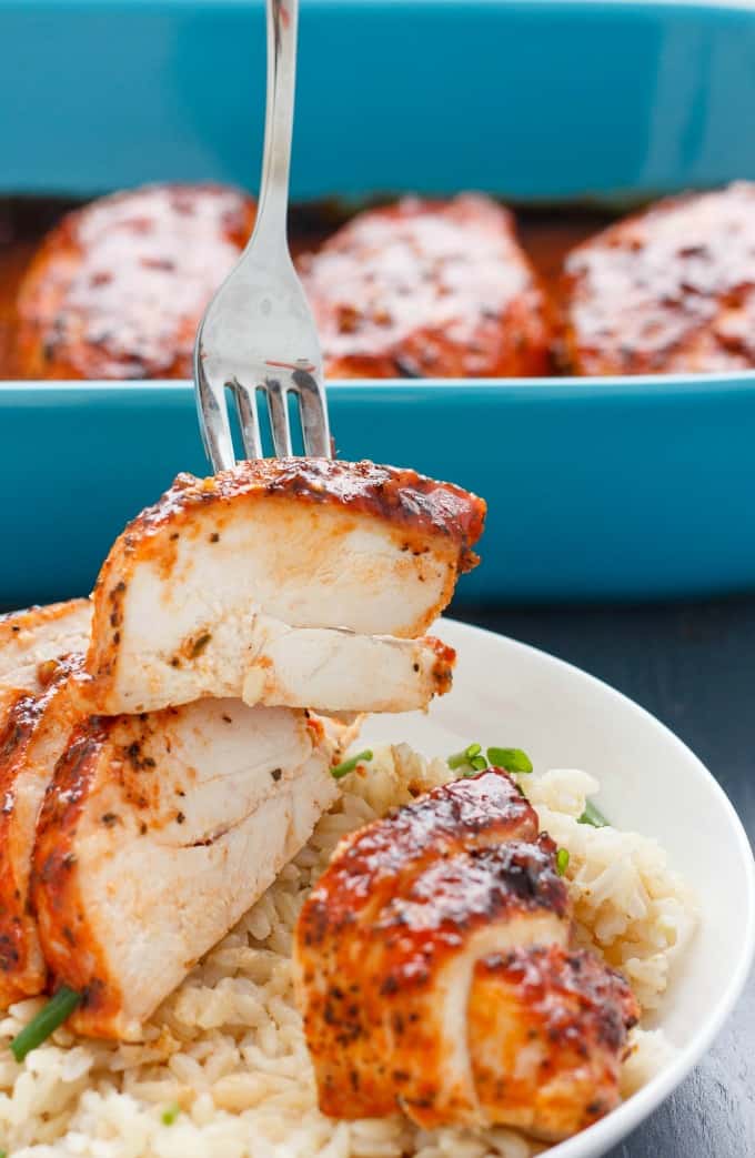 Sliced Sriracha chicken breasts with rice and veggies on white plate, blue baking pot in the background