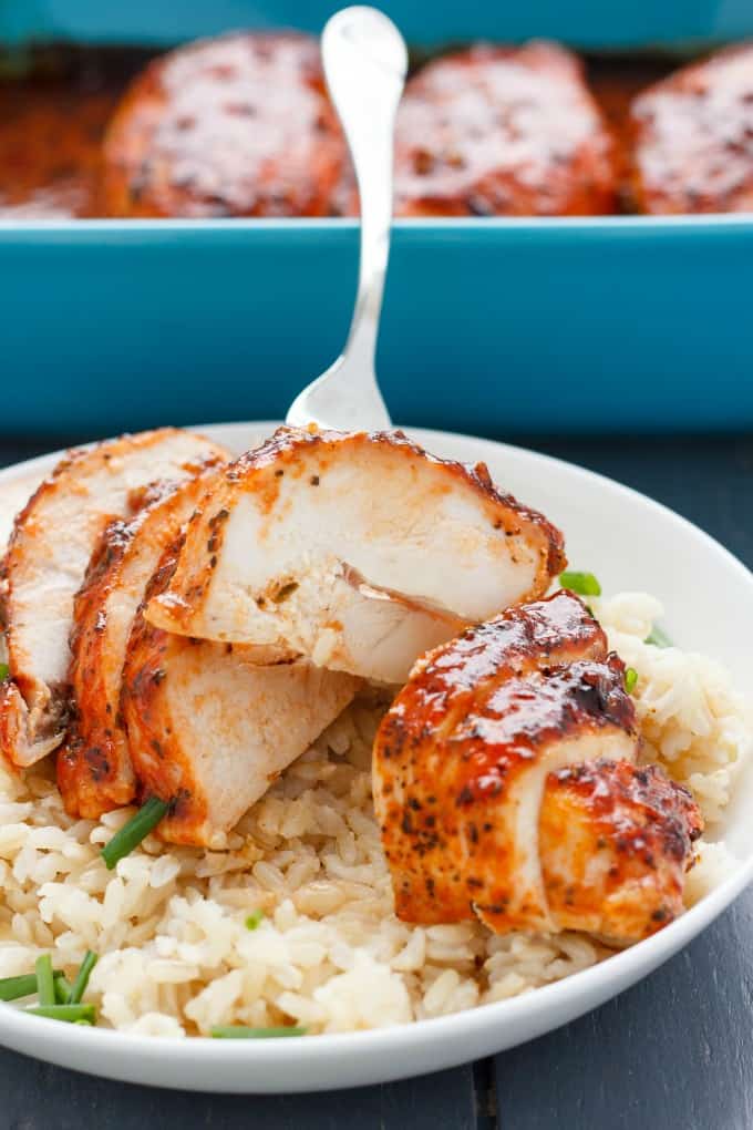 Sriracha sliced chicken breast with rice and veggies picked by fork on white plate, blue baking pot in the background