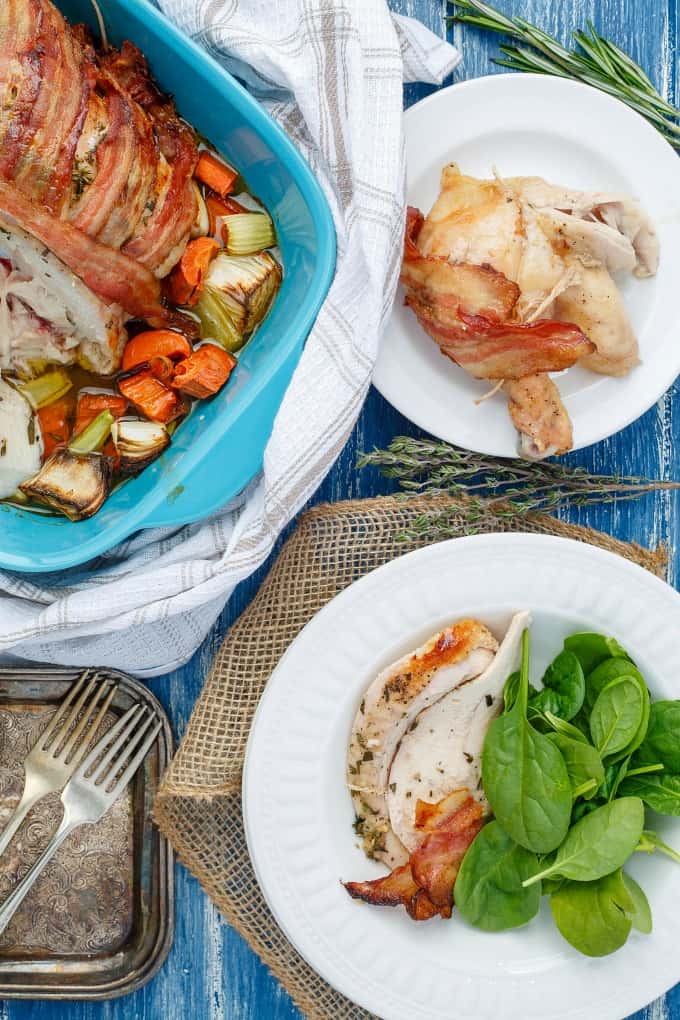 Bacon Wrapped Whole Chicken with Maple-Herb Butter on white plates and in baking pot with veggies on blue table with forks