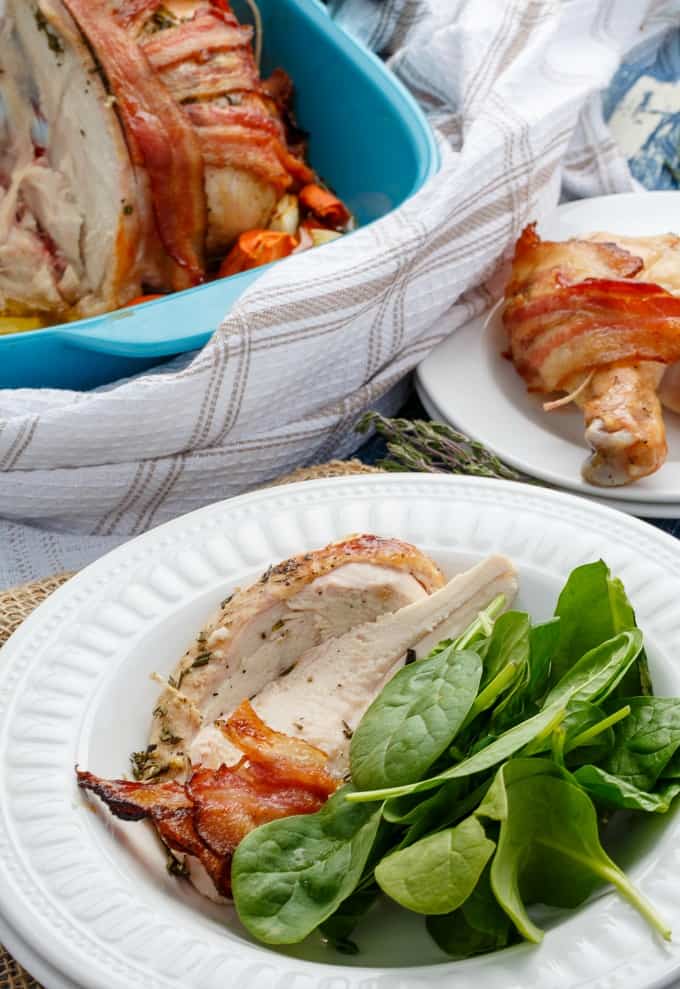 Bacon Wrapped Whole Chicken with Maple-Herb Butter on white plates with veggies , same dish in blue baking pot