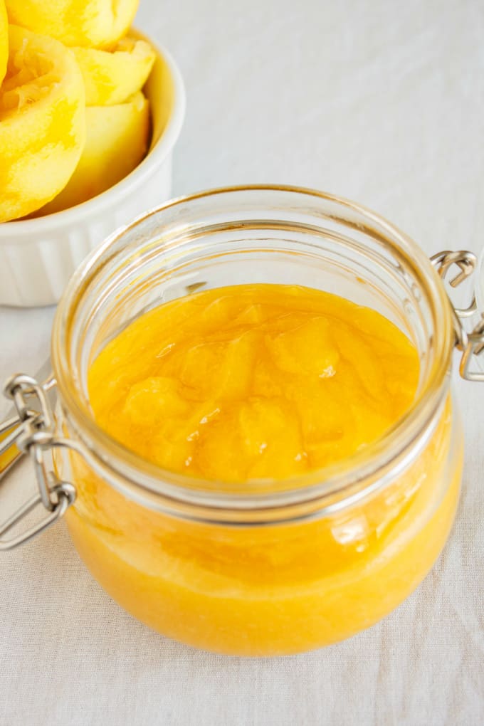 Brown Butter Lemon Curd in glass jar next to bowl of lemons on white background