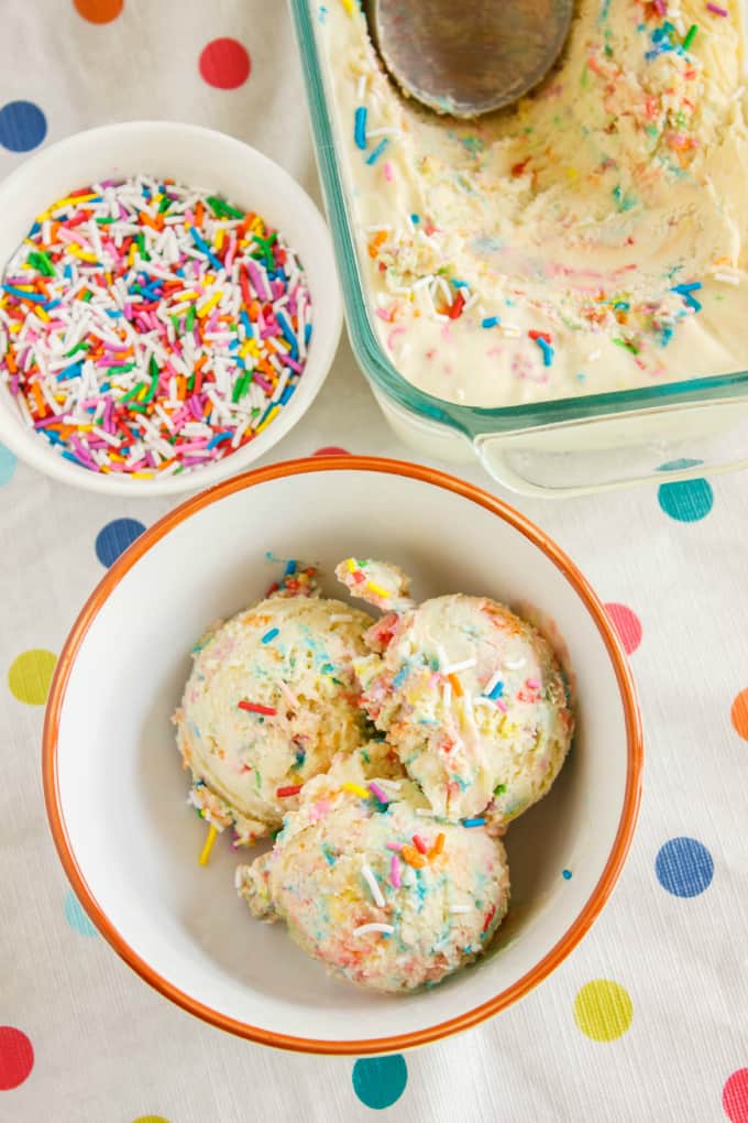 Homemade Birthday Cake Ice Cream on glass container with icecream spoon, in orange white bowl and bowl with candy sprinkles