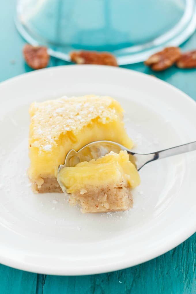 Pecan and Lemon Bar on white plate with spoon on blue table with spilled pekans