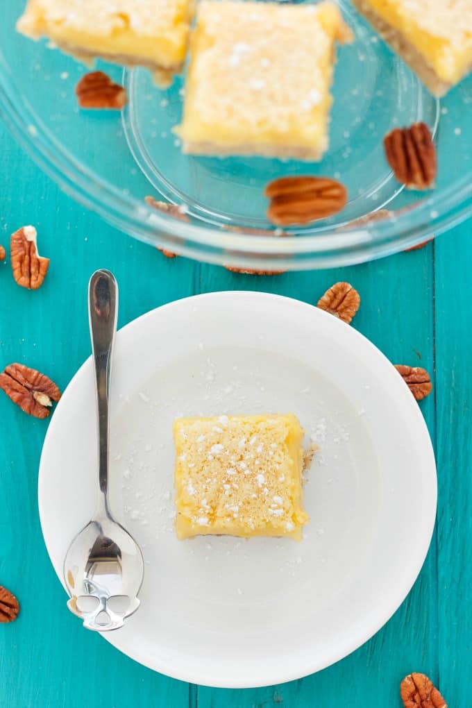 Pecan and Lemon Bars on glass trray and lemon bar on white plate with spoon on blue table with spilled pekans around#vegetarian