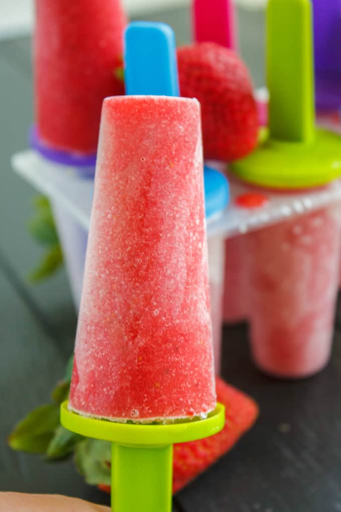 Strawberry Sorbet Popsicle, popsicles in plastic form and ripe strawberry in the background