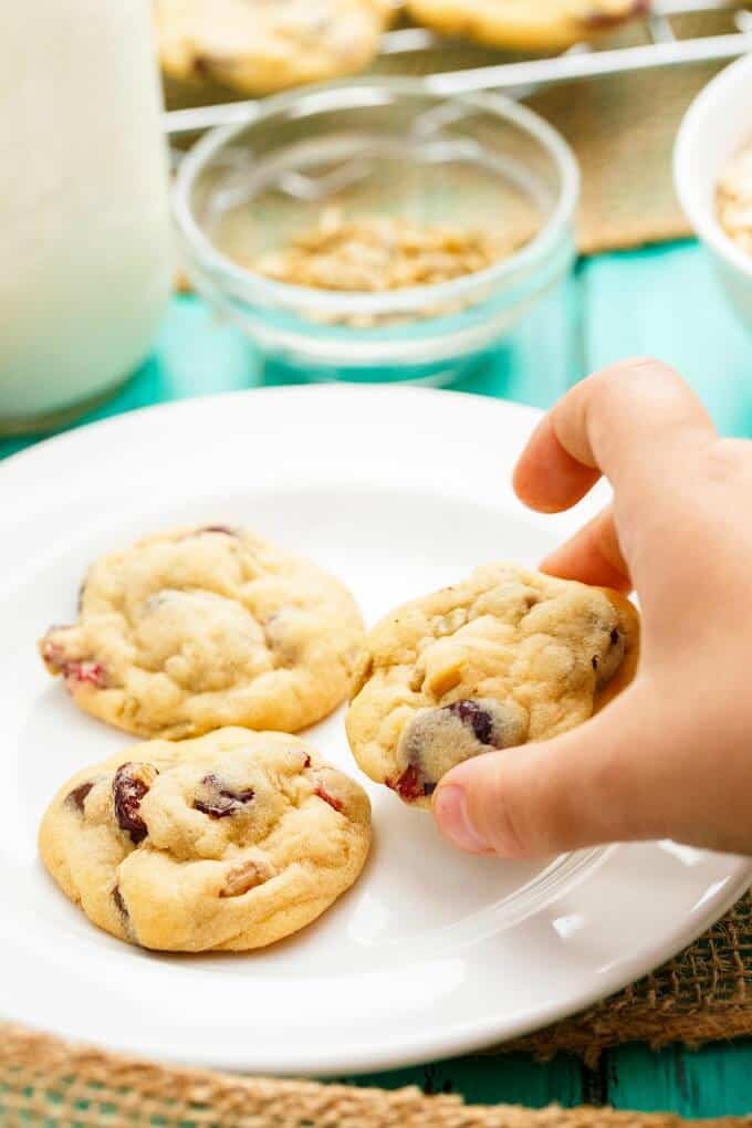 Granola Bar Chocolate Chip Cookies held by hand on white plate, bowls of ingredients 