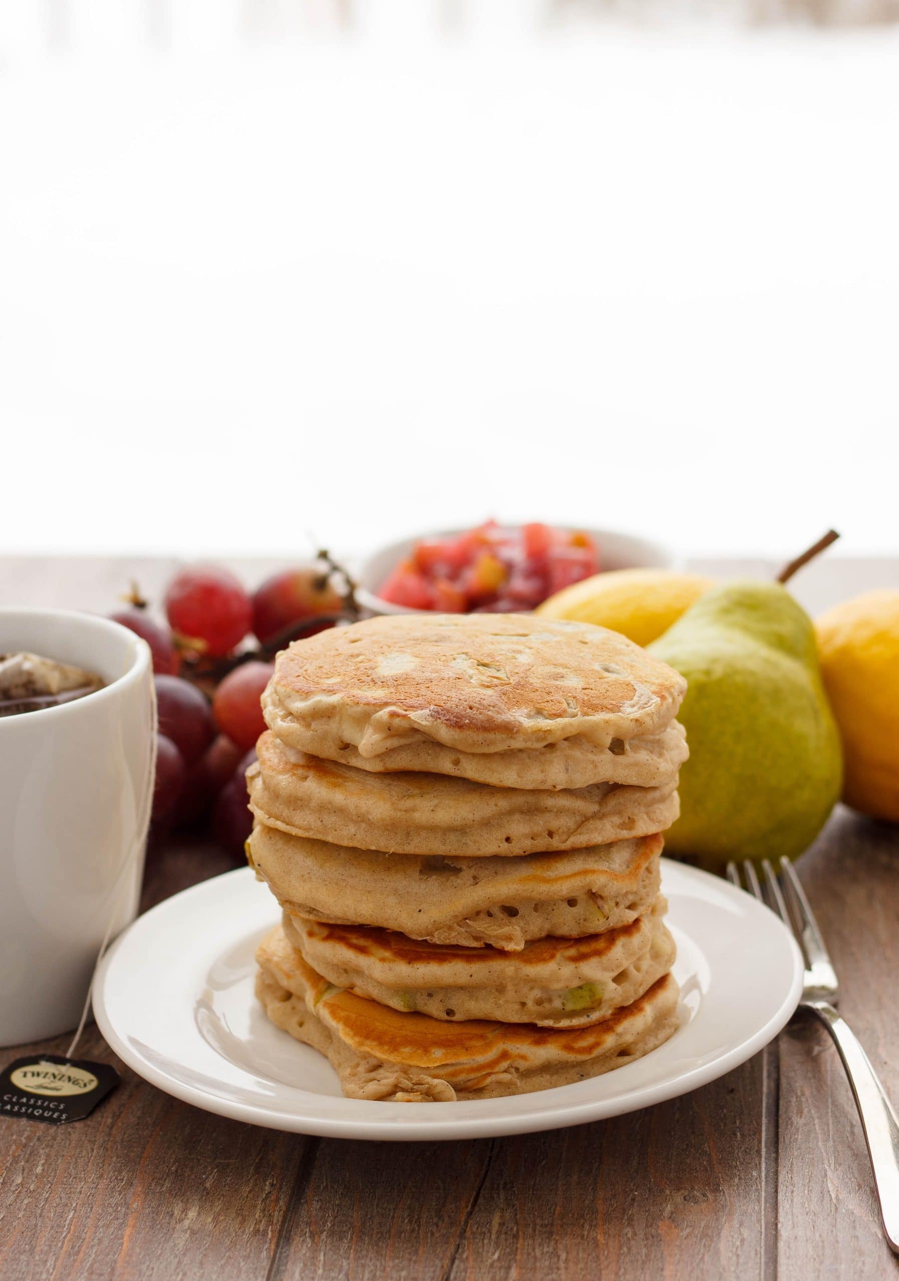 Pear Pancakes with Grape Sauce on white plare next to fork, grapes, peach and lemons in the background