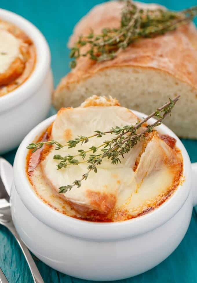 Massaman Curry French Onion Soup in white bowl on blue table with spoon and loaf of bread with herbs