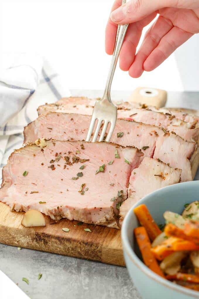 Pork Shoulder with Vegetables sliced on wooden pad, hand holding fork, vegetable in bowl