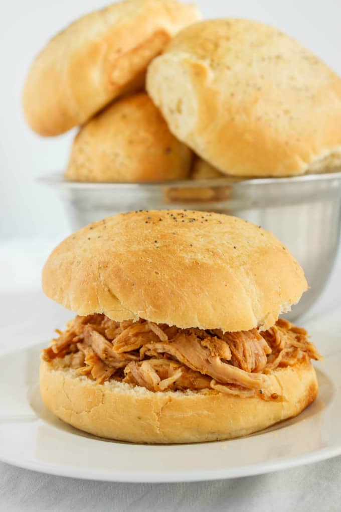 Pulled Pork in the Slow Cooker between buns on white plate, bowl of buns in the background