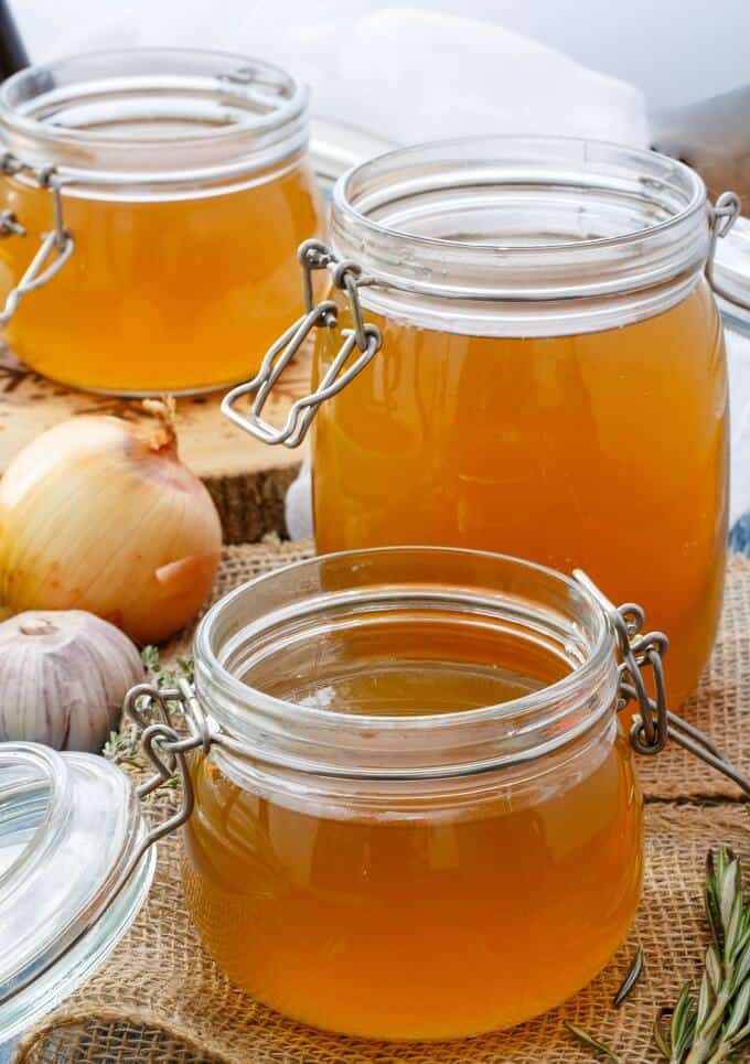 Homemade Chicken Stock in glass jars with onion,garlic and herb on table