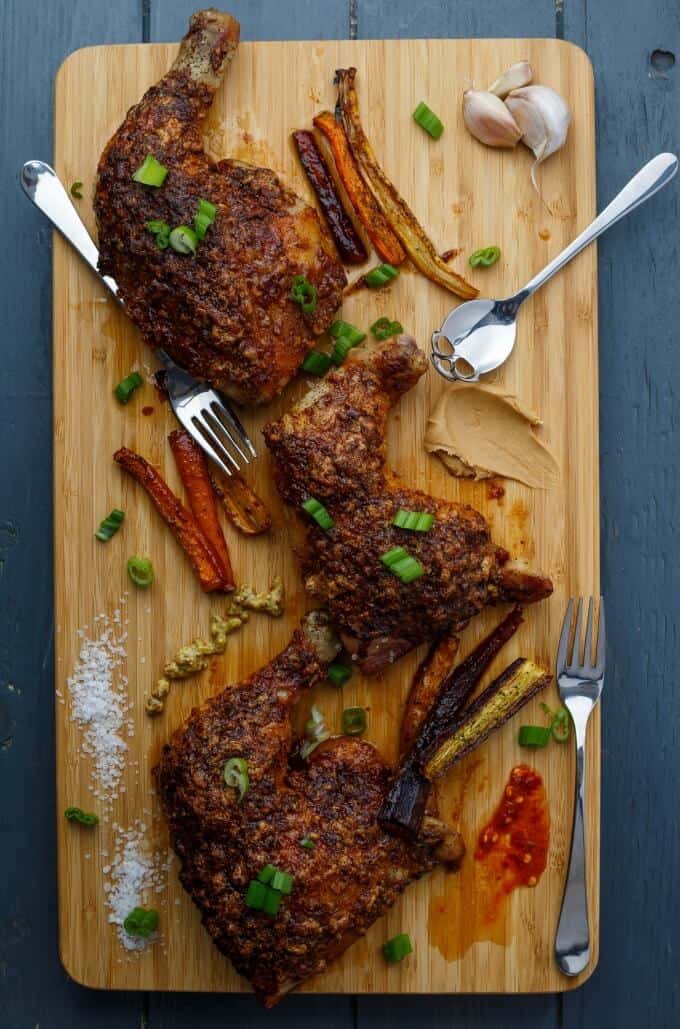 Asian Inspired Chicken Leg Quarters on wooden pad with veggies, garlic, forks and spoon