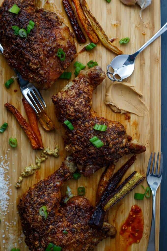 Asian Inspired Chicken Leg Quarters on wooden pad with forks, spoon and sliced veggies