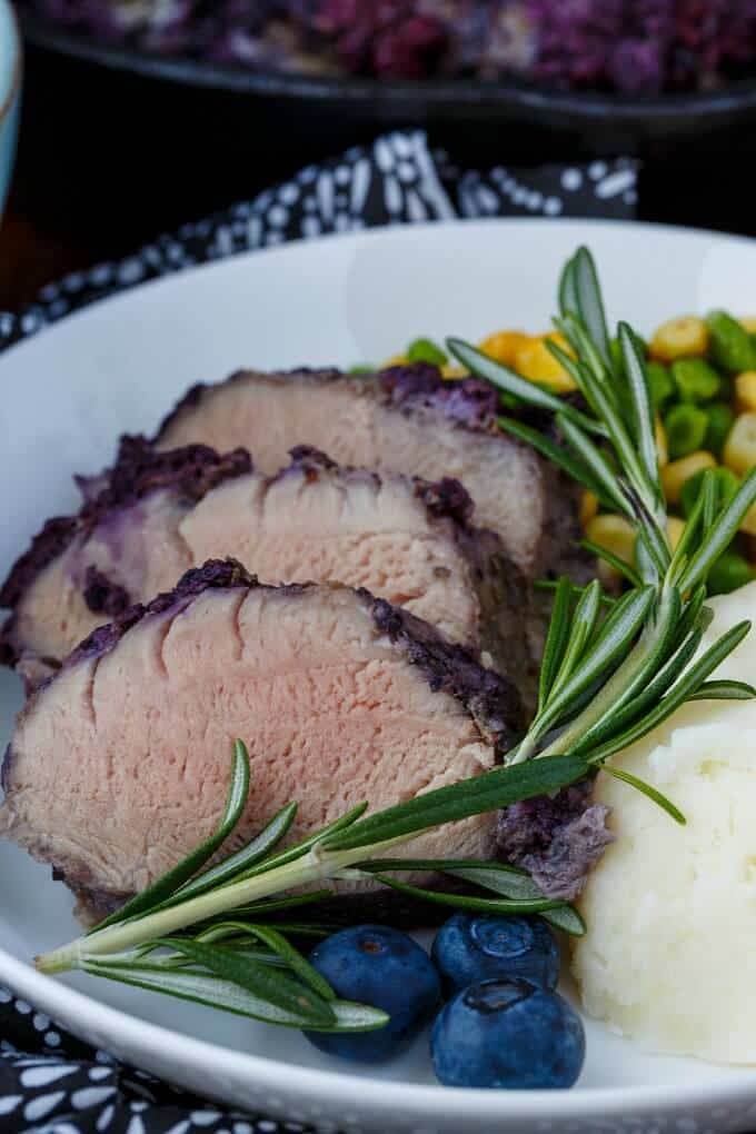 Blueberry Molasses Pork Tenderloin on white plate with fruits,herb,veggies and side dish