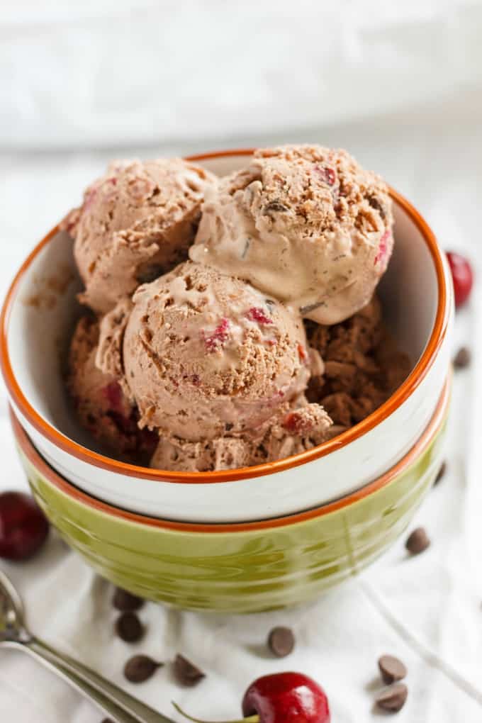 Cherry-Chocolate Ice Cream in pile of bowls on white table with spoon, chocolate chips and cherries