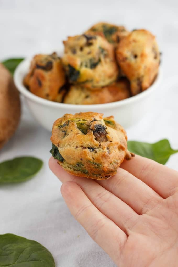 Mushroom and Spinach Puffs in white bowl and one piece held by hand, leave s on white table