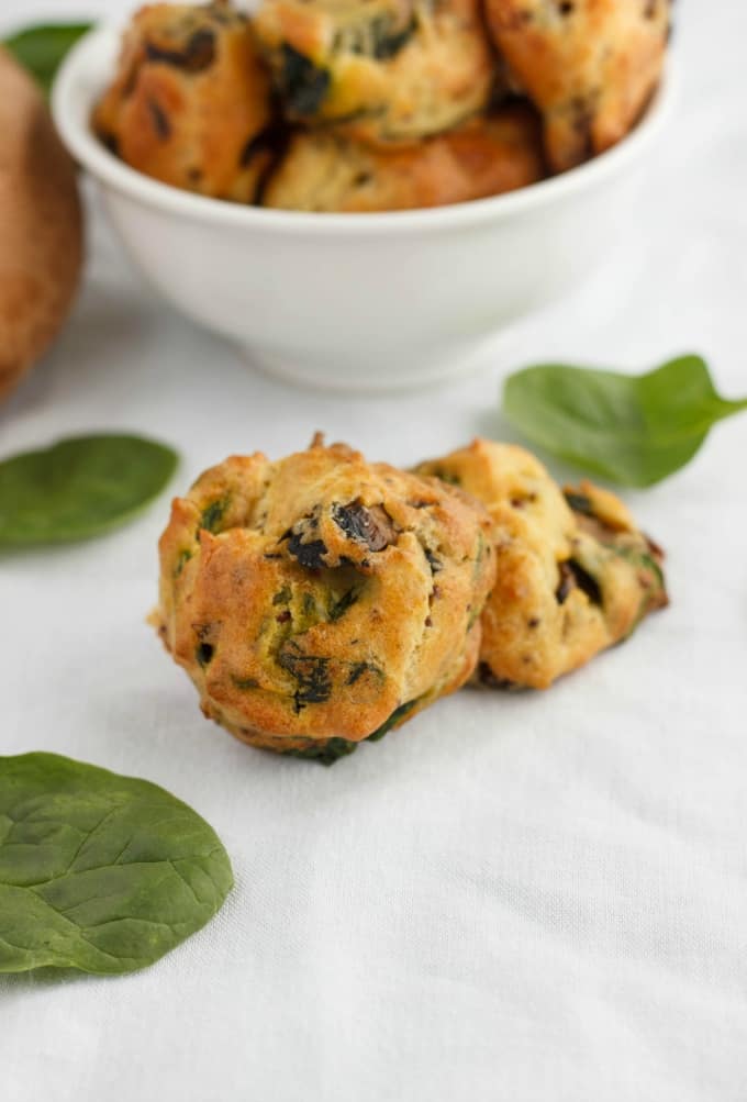 Mushroom and Spinach Puffs on white table with spilled spinach, bowl full of puffs in the background