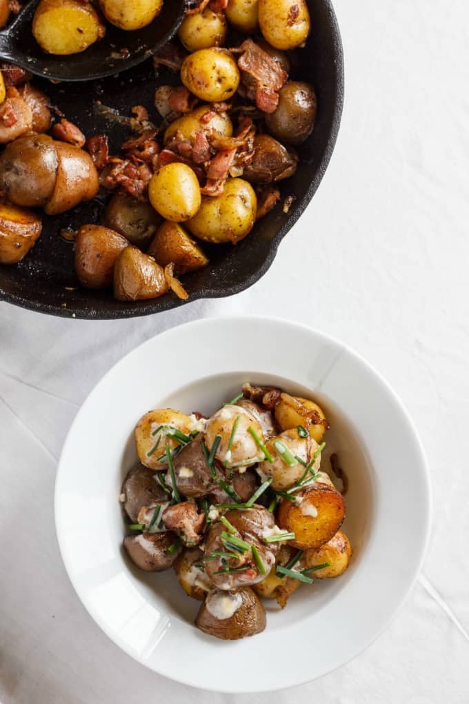 Potatoes and bacon with yogurt-chive sauce on white plate and in black pan on white table