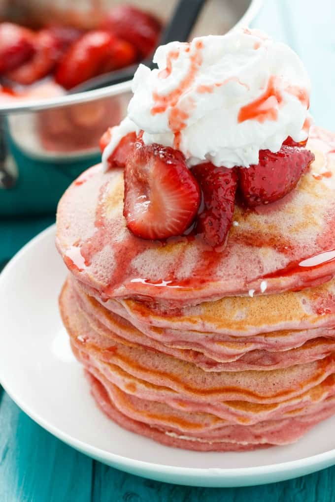 Strawberries and Cream Pancakes on white plate, pot with strawberries in the background