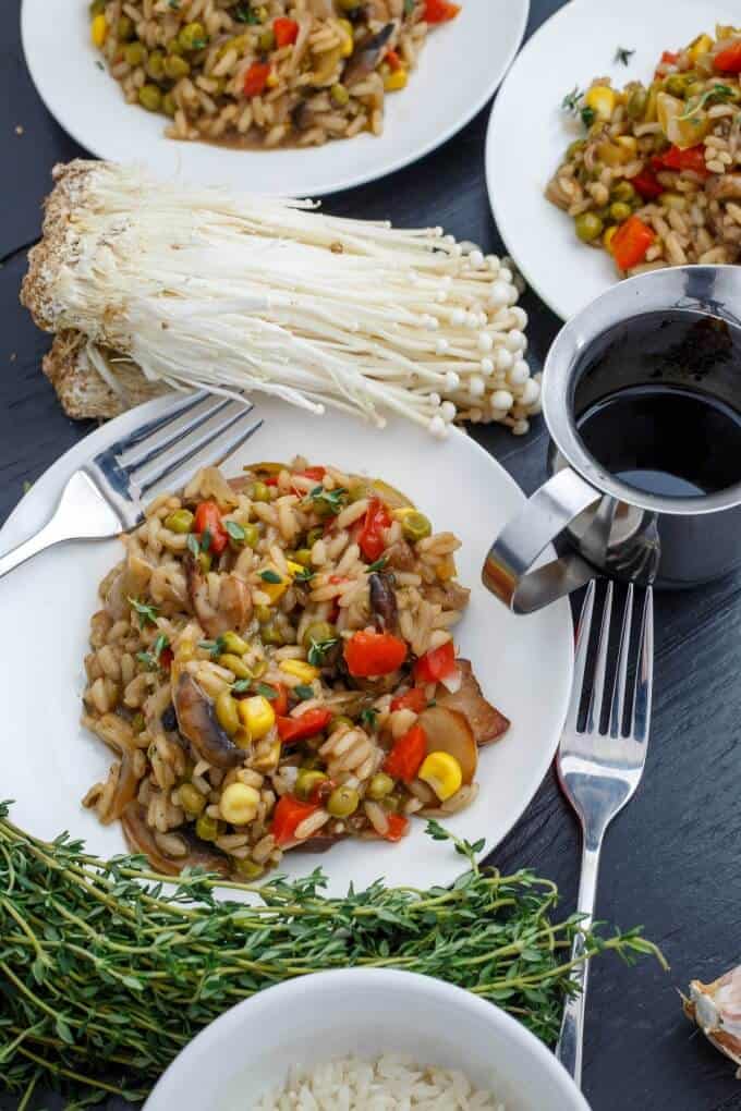 Vegetable Risotto with Homemade Chicken Stock on white plate with works, mushrooms, herbs on black table