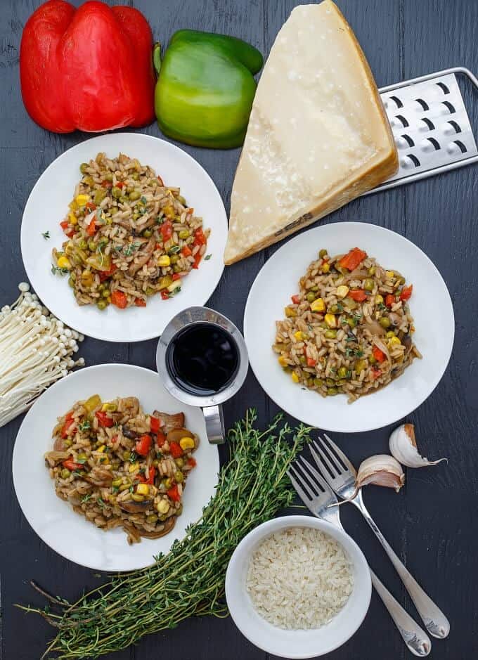 Vegetable Risotto with Homemade Chicken Stock on white plates on gray table with forks, mushrooms, herbs, cheese, grater, rice, garlic, vegetables