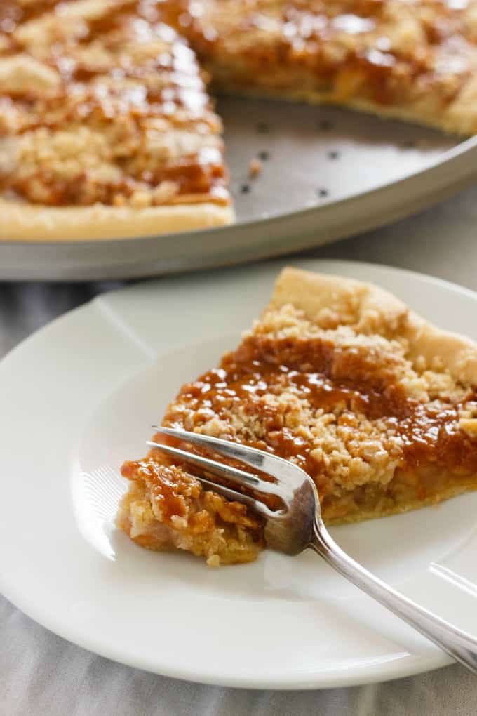 Apple Crisp Pizza  slice cutted by fork on white plate, rest of pizza on tray