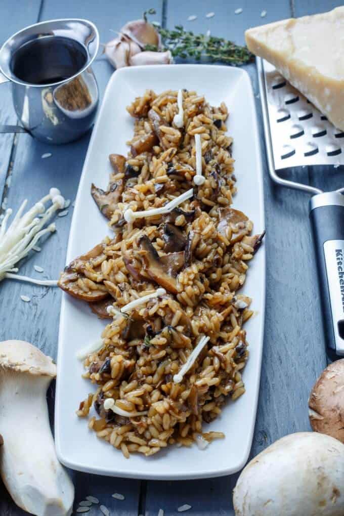 Balsamic Mushroom Risotto on white tray on black table with mushrooms, cheese, grater, garlic, herbs and sauce