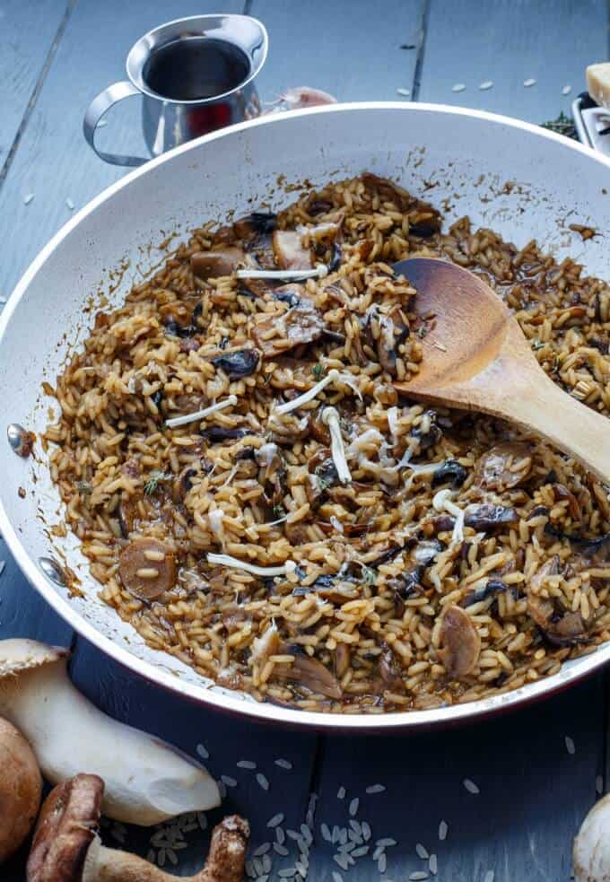 Balsamic Mushroom Risotto in pan with wooden spatula on black table with mushrooms and jar with sauce