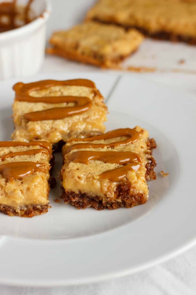 Banana Bread Bars with a Peanut Butter-Molasses Drizzle  on white plate, rest of dessert in the background