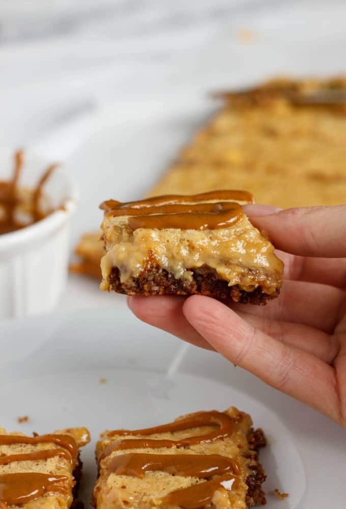 Banana Bread Bars with a Peanut Butter-Molasses Drizzle on white plate and one held by hand, rest of dessert in the background