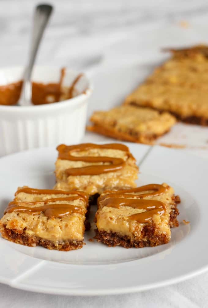 Banana Bread Bars with a Peanut Butter-Molasses Drizzle on white plate, rest of dessert in the background with drizle in white bowl and spoon
