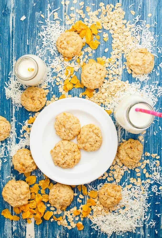 Forest Ranger Cookies on white plate and blue table with spilled ingredients around with two glass jars full of milk and pink straw