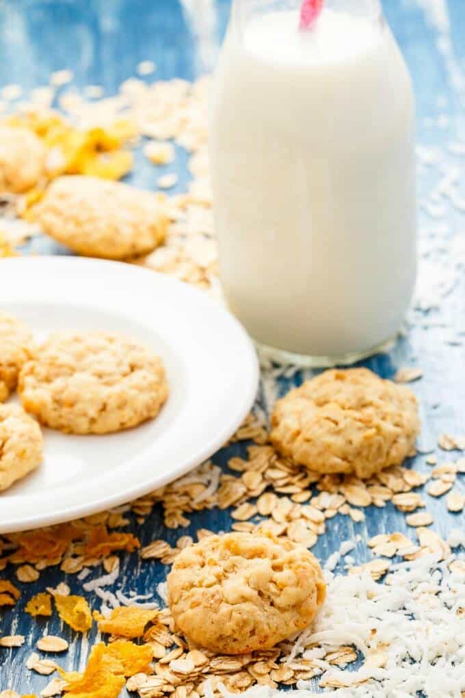 Forest Ranger Cookies on white plate and blue table with spilled ingredients around with glass jar full of milk with pink straw