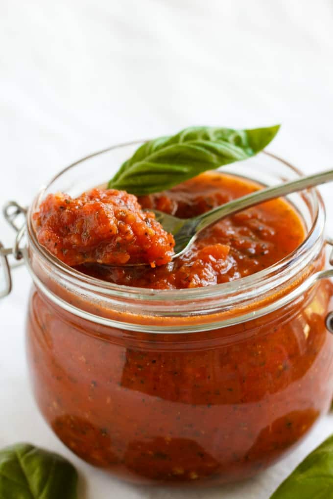 Herb Pizza Sauce  in glass jar picked by spoon, herbs spilled around