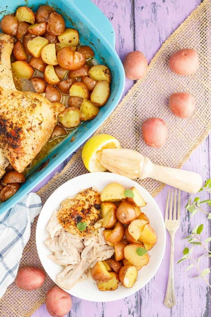 One-Pan Lemon Chicken Leg Quarters with Creamer Potatoes in blue casserole and on white plate. Scattered potatoes, half lemon, herbs, fork, wooden kitchen tool, cloth wipe on purple table