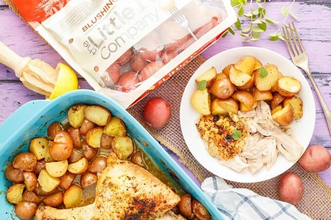 One-Pan Lemon Chicken Leg Quarters with Creamer Potatoes on white plate and blue baking pot on puple table with potatoes, sack of potatoes , fork , lemon, herbs