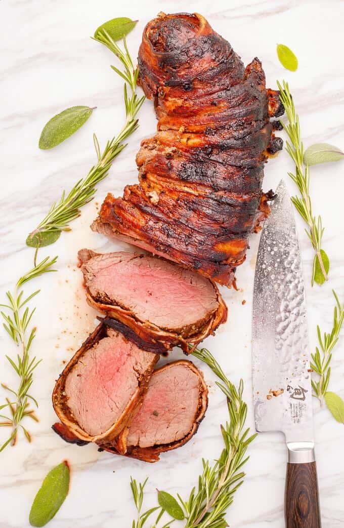 Bacon-Wrapped Balsamic and Rosemary Beef Tenderloin with herbs and knife