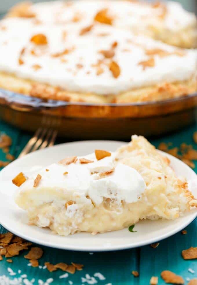 Gluten-Free Coconut Cream Pie slice on white plate, rest of cake on tray in the background