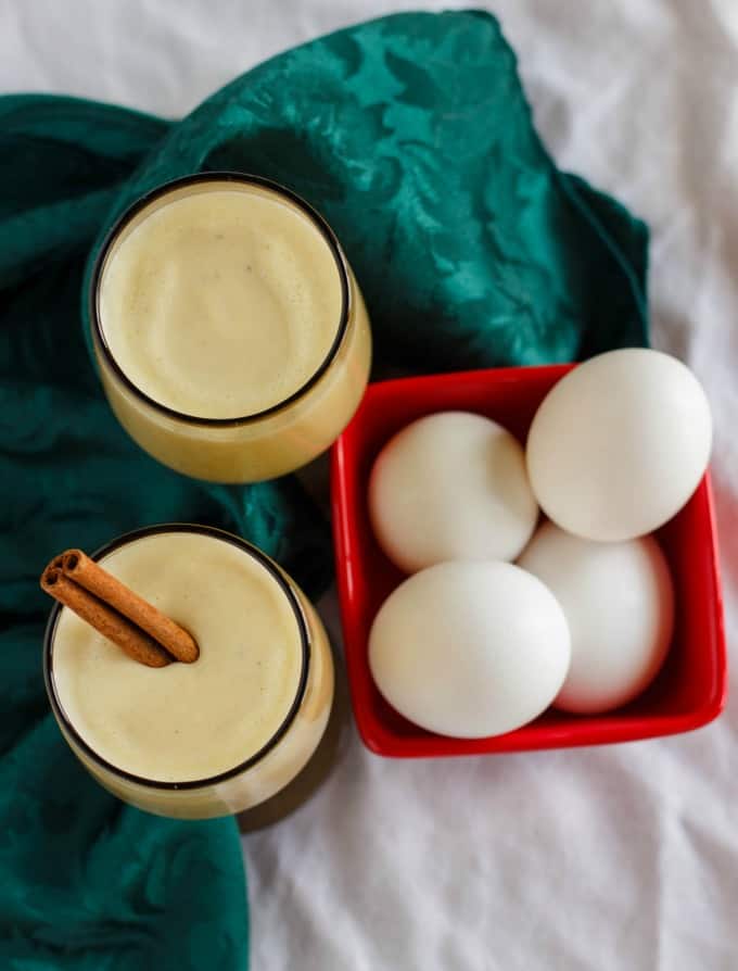 Homemade Eggnog using Leftover Egg Yolks  in glass cups next to red container with eggs and green cloth