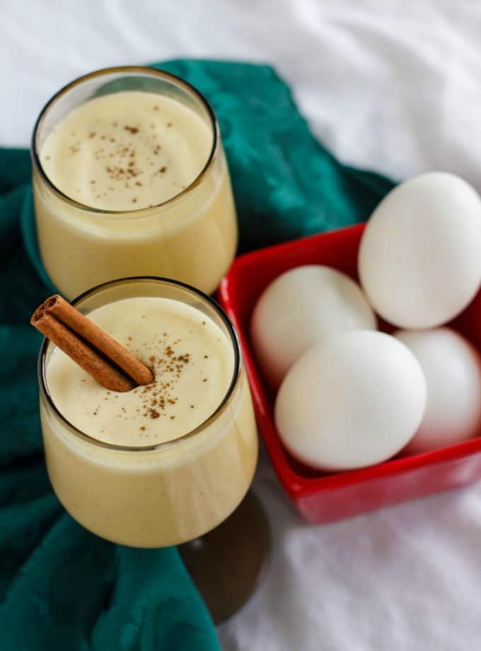 Homemade Eggnog using Leftover Egg Yolks in glass cups next to red container with eggs and green cloth