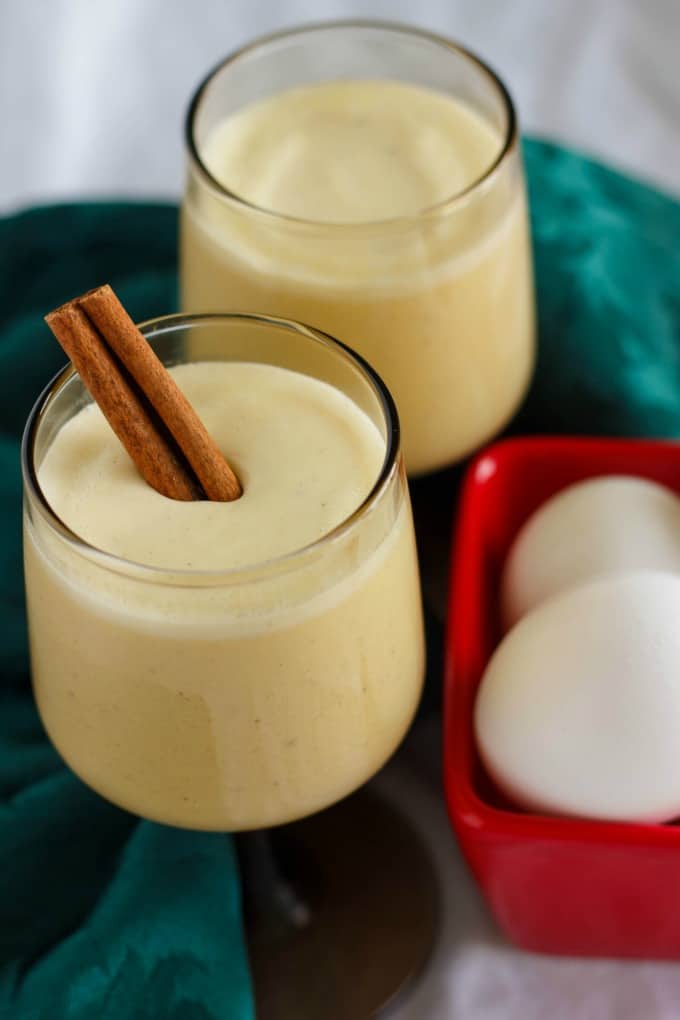 Homemade Eggnog using Leftover Egg Yolks in white glass cups next to red container with eggs and green cloth