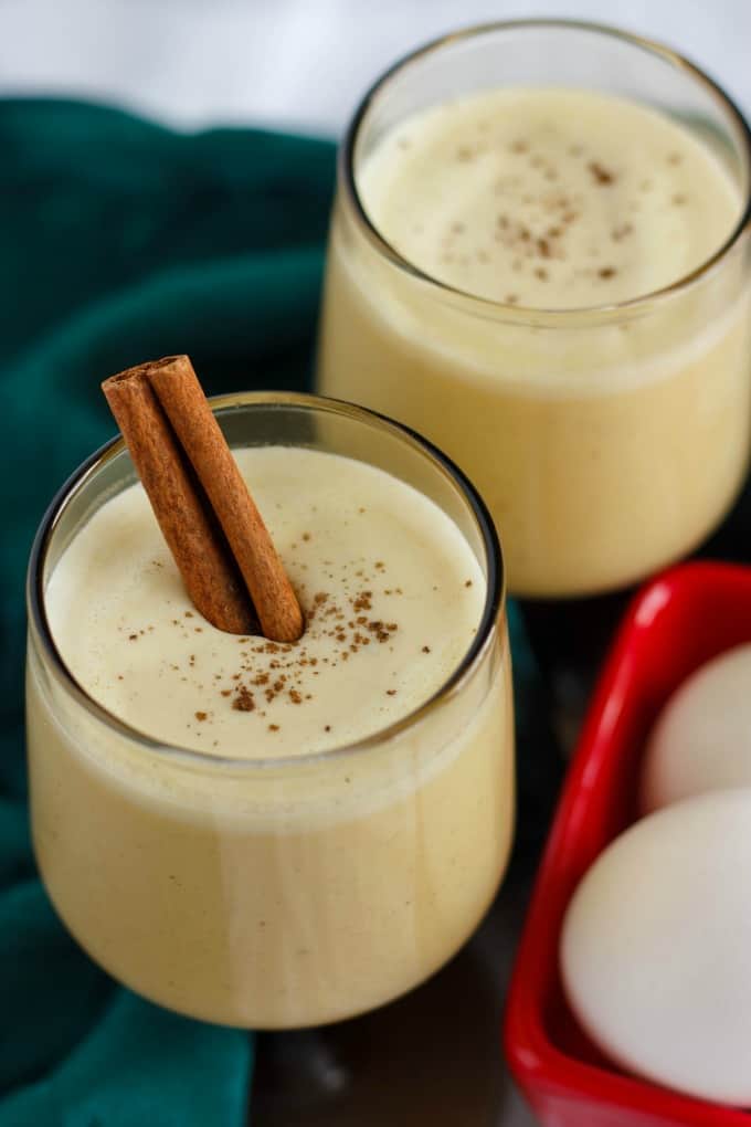 Homemade Eggnog using Leftover Egg Yolks in glass cups next to red container with eggs and green cloth