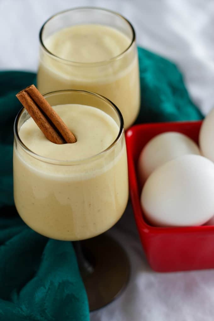 Homemade Eggnog using Leftover Egg Yolks in glass cups next to red container with eggs and green cloth