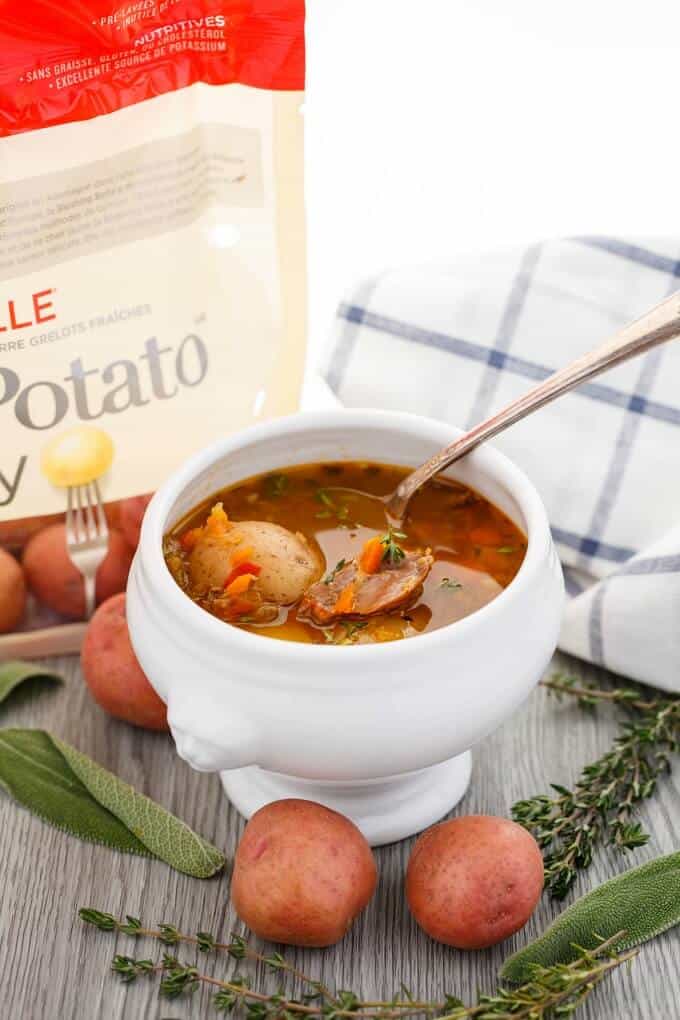 Homemade Turkey Soup with Creamer Potatoes in white bowl with spoon on table with sack of potatoes, herbs and potatoes