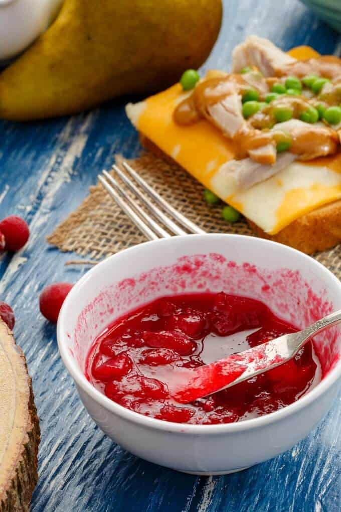 Pear Cranberry Sauce in white bowl on blue table with fork, sandwich and cranberries 