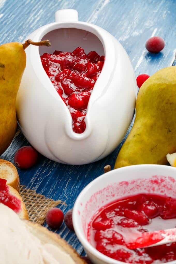 Pear Cranberry Sauce in white bowls on blue table with cranberries, peaches