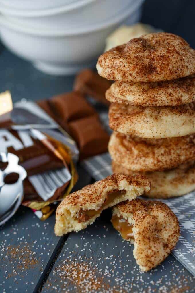 Caramilk Stuffed Snickerdoodles on gray tablw with chocolate, spoon and white bowls in the background